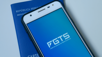 celular com fundo azul e a sigla FGTS referente à Contribuição Social, e uma carteira de trabalho azul ao fundo
