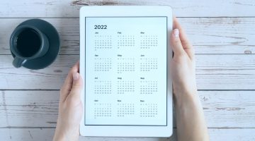 fundo de madeira clara, com uma xícara e café à esquerda e um tablet com calendário de 2022 centralizado, fazendo menção ao prazo de entrega da ECF