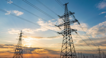 céu azul com nuances de laranja, com cabos e torres de operações de energia e telecomunicações